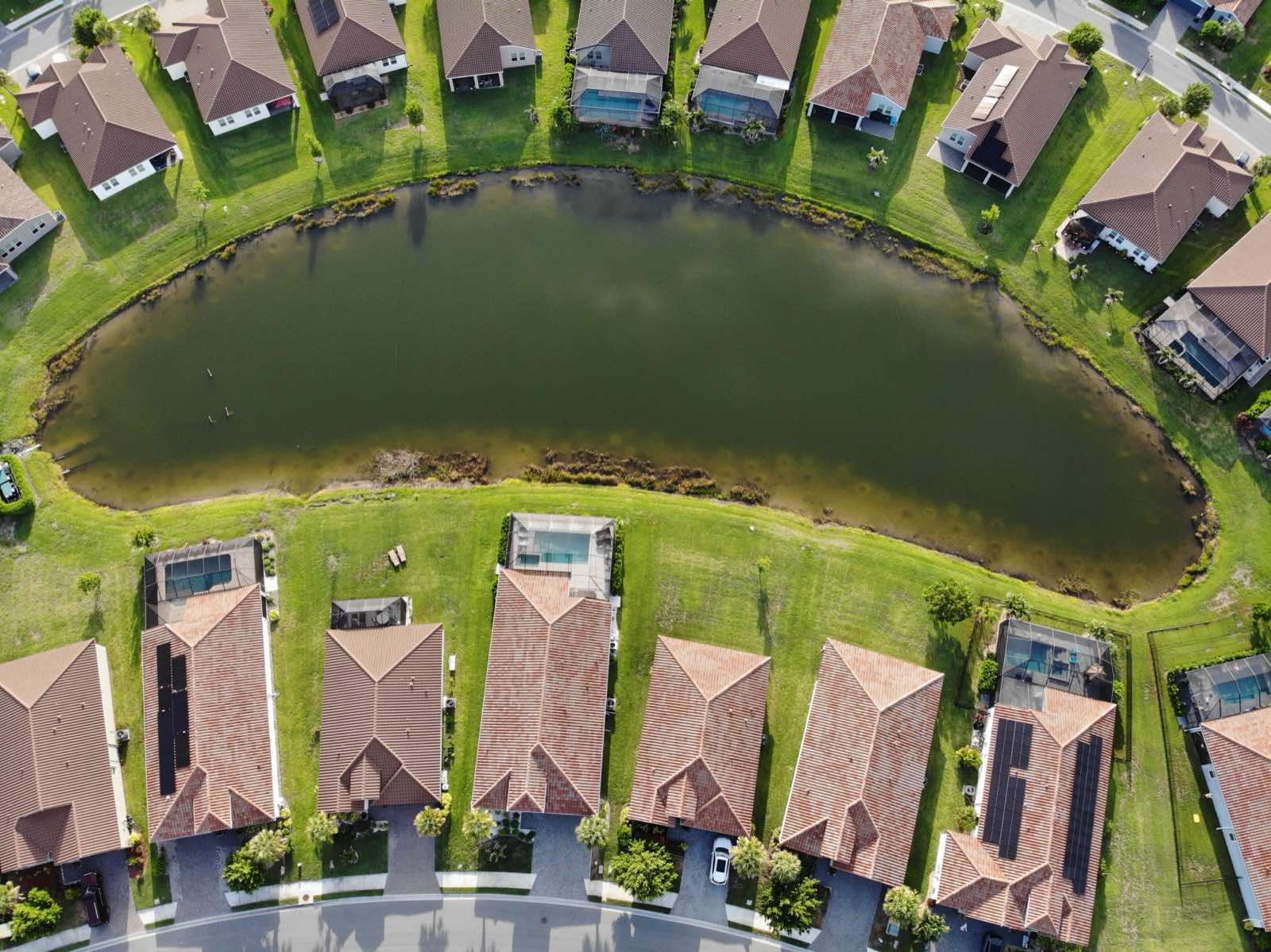 Aerial capture of a crescent-shaped stormwater pond with open water and a mowed grass bank running to the shoreline.